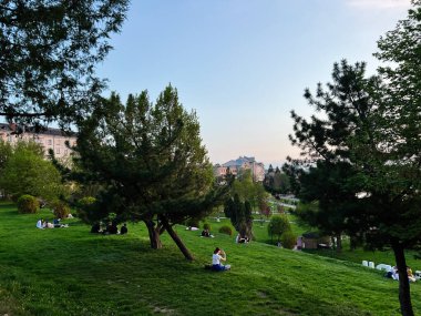 Ternpil, Ukrayna - 23 Nisan 2025: Ağaçların altında dinlenen insanlar, arka planda kentsel binalar.