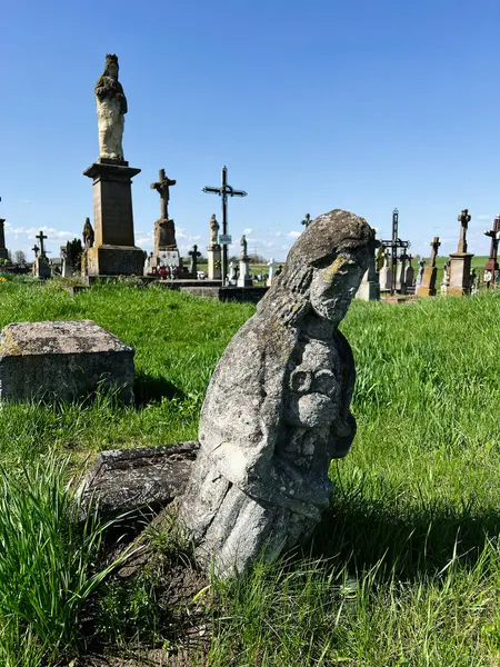 Khorostkiv, Ukrayna - 23 Nisan 2025: Çimenli bir arazide yıpranmış mezarların ve heykellerin yer aldığı sakin bir mezarlık sahnesi