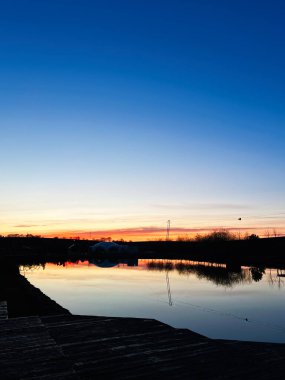 Gün batımının sakin bir akşam sahnesi sakin suların üzerine yansıyor..