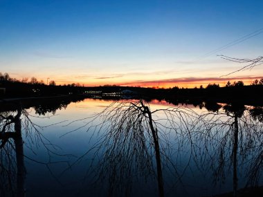 Huzurlu alacakaranlık sahnesi yansıyan bir gölet ve uzak, canlı günbatımı renkleriyle