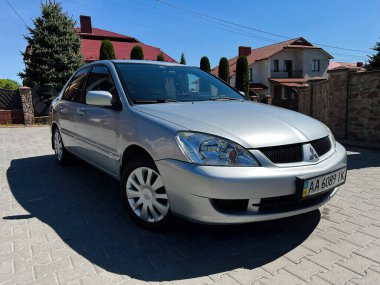 Kyiv, Ukrayna - 28 Nisan 2025: Güneşli mahallelerde evleri ve ağaçları olan gümüş renkli Mitsubishi Lancer Sedan aracı.