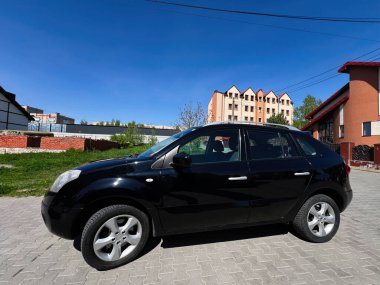 Kyiv, Ukrayna - 28 Nisan 2025: Siyah Renault Koleos SUV iskan binaları ve yeşilliklerin olduğu asfalt bir alana park edildi