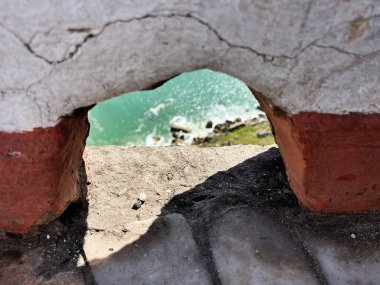 Portekiz, Nazare 'de eski bir taş duvarın içinden görünen turkuaz su.