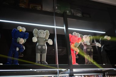 Ivano-Frankivsk, Ukrayna - 29 Nisan 2025: Dekoratif KAWS sanat figürleri canlı renkler ve aydınlatma ile cam bir ekrana yerleştirildi