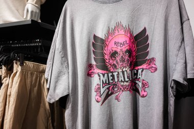Ivano-Frankivsk, Ukrayna - 29 Nisan 2025: Gri tişört Metallica bir perakende satış ortamında pembe kafatası ve kanat tasarımı sergiliyor