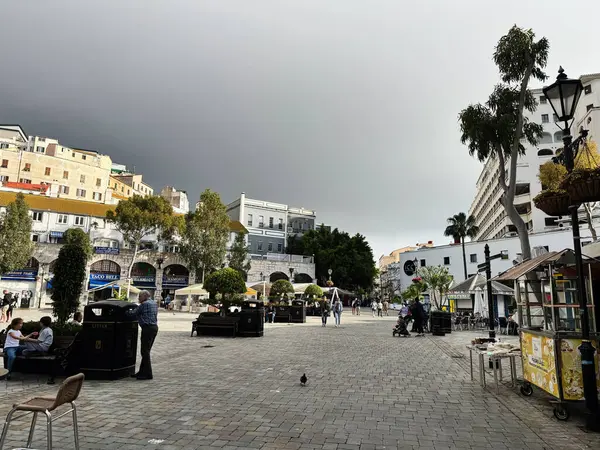 Cebelitarık, İngiltere - 01 Mayıs 2025: Taş kaldırımlı, ağaçlı, insanlı ve bulutlu gökyüzü olan Cebelitarık Meydanı.