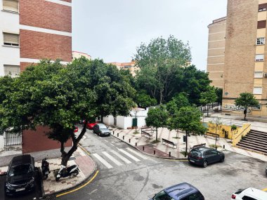 Malaga, İspanya - 02 Mayıs 2025: Büyüleyici şehir caddesi, yemyeşil ağaçları, park edilmiş araçları ve Malaga kentsel mimarisi.