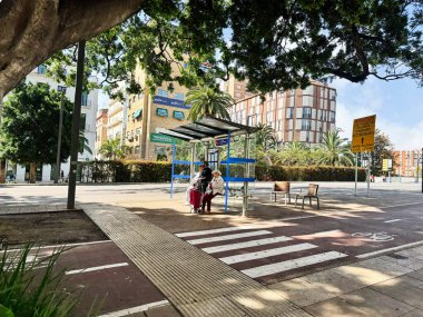 Malaga, İspanya - 02 Mayıs 2025: İspanya 'nın Malaga şehrinde büyük ağaçların gölgelediği bir otobüs durağı.