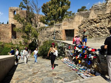 Malaga, İspanya - 02 Mayıs 2025: Malaga, İspanya 'da tarihi kalıntıların arasında yürüyen turistler bir hediyelik eşya tezgahının yanında