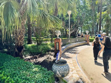 Malaga, İspanya - 02 Mayıs 2025: İspanya 'nın Malaga şehrinde tropik bitkiler ve ziyaretçilerle dolu huzurlu bir park yolu.