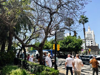 Malaga, İspanya - 02 Mayıs 2025: İspanya 'nın Malaga şehrinde insanlar parlak güneş ışığı altında yeşilliğin yakınında yürüyorlar