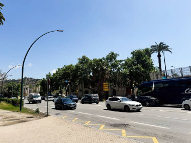 Malaga, İspanya - 02 Mayıs 2025: Malaga, İspanya 'da güneşli bir bulvar boyunca araç ve ağaçların yer aldığı şehir sahnesi