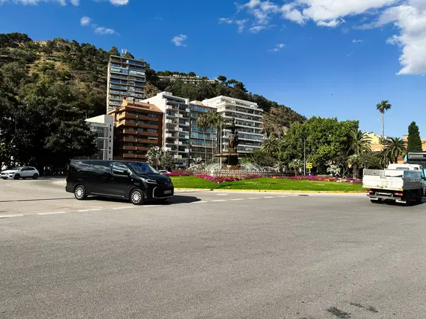 Malaga, İspanya - 02 Mayıs 2025: Malaga 'da çeşme, çiçek yatakları ve şehir manzaralı bir kavşak