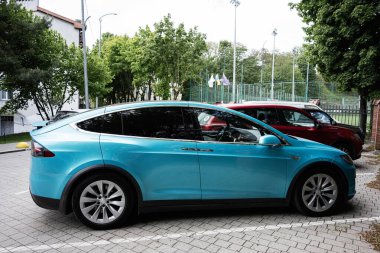 Lviv, Ukrayna - Mayıs 04, 2025: Turkuaz Tesla Model Y elektrikli araç yeşil park ve kentsel çevre yakınlarına park edildi