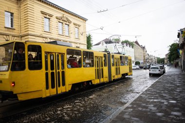 Lviv, Ukrayna - 04 Mayıs 2025: Lviv, Ukrayna 'da çevreleyen şehir binalarının bulunduğu bir kaldırım taşından geçen sarı bir tramvay. 