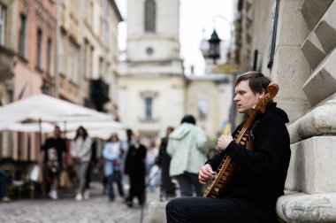 Lviv, Ukrayna - 04 Mayıs 2025: Lviv, Ukrayna 'da kalabalık bir şehirde otururken bandura müzik aleti çalan bir adam. 