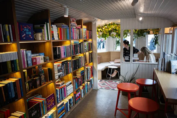 Lviv, Ukrayna - 04 Mayıs 2025: Kitaplarla dolu ahşap raflar ve masalarla dolu rahat bir oturma alanı