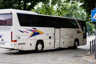 Lviv, Ukrayna - 04 Mayıs 2025: Yeşillik ağaçların yakınındaki kaldırım taşı yolda park etmiş beyaz bir otobüs.