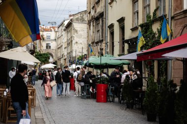 Lviv, Ukrayna - 04 Mayıs 2025: Açık kafeler, Ukrayna bayrakları ve Lviv, Ukrayna 'da büyüleyici bir şehir ortamındaki insanların yer aldığı sokak manzarası. 