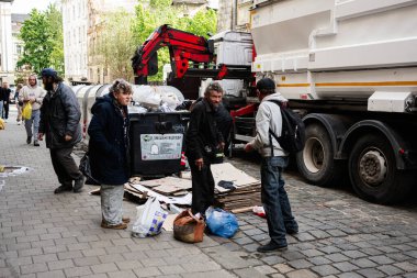 Lviv, Ukrayna - 4 Mayıs 2025: İnsanlar Lviv, Ukrayna 'da işlek bir kentsel caddede çöp kamyonunun yanında geri dönüşümlü materyalleri sıralayan dilenciler. 