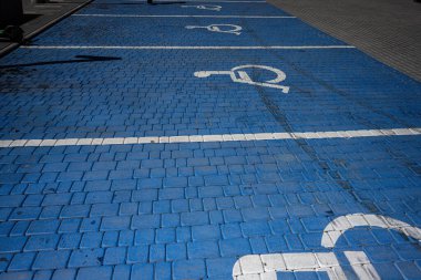 Mavi kaldırım taşı yüzeyinde açık engelli işaretleri olan ulaşılabilir park yerleri