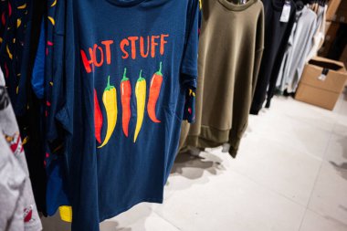 Renkli chili Hot Stuff tasarımlı şık grafik tişörtler bir giyim mağazasında sergileniyor. 