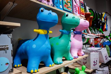 Üç canlı dinozor oyuncağı bir oyuncakçıda rengarenk bir arkaplana karşı dizilmiş.