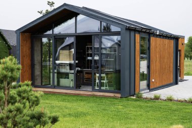 Camdan duvarları ve peyzajlı yeşil çevresi olan prefabrik modern bir ev.