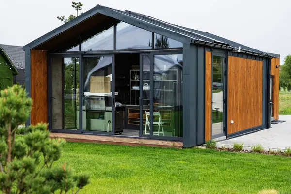 Camdan duvarları ve peyzajlı yeşil çevresi olan prefabrik modern bir ev.