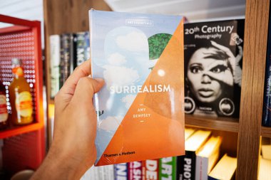 Lviv, Ukrayna - 04 Mayıs 2025: Amy Dempsley, Sürrealizm. Sürrealizm hakkında bir kitap sergileyen bir kişi, çeşitli başlıkları içeren kitaplıklar.