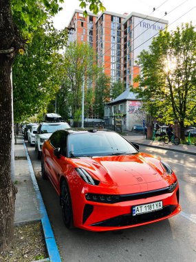 Ivano-Frankivsk, Ukrayna - 14 Mayıs 2025: Şehir caddesi boyunca park edilmiş turuncu spor araç yüksek binalar ve yeşil yeşillikler