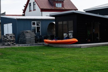 Akranes, İzlanda - 15 Mayıs 2025: Çağdaş bir ev, siyah bir kulübe ve dışarıda turuncu bir kano ile çimenlik.