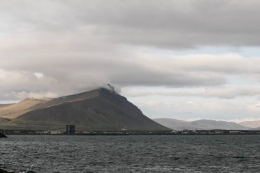 Dağlı, okyanuslu ve bulutlu gökyüzü olan İzlanda kıyı şeridinin huzurlu manzarası
