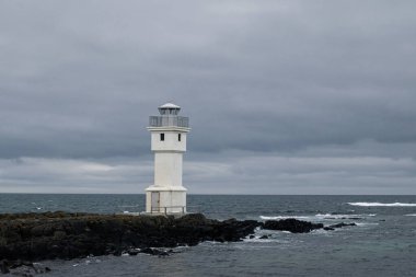 Akranes, İzlanda yakınlarındaki bulutlu bir günde okyanus kenarındaki beyaz deniz feneri dinginliği vurguluyor