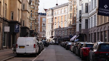 Kopenhag, Danimarka - 21 Nisan 2025: Kopenhag, Danimarka 'da geleneksel binaların ve park halindeki arabaların yer aldığı Cozy Caddesi.