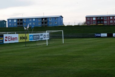 Akranes, İzlanda - 16 Mayıs 2025: Reklamlarla ve renkli İskandinav tarzı binaların arkaplanlarıyla açık futbol sahası