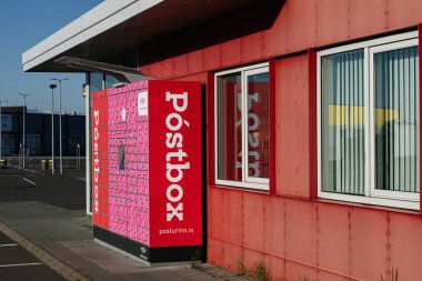 Akranes, İzlanda - 16 Mayıs 2025: Akranes, İzlanda 'da günışığında modern bir binanın yanındaki kırmızı posta kutusu.