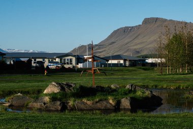Yeşillik, evler ve dağlık bir arkaplan içeren Akranes ve İzlanda manzarası.