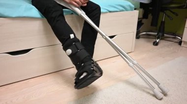 Kırık bacaklı bir çocuk yatakta oturuyor. Koltuk değneği kullanıyor. Ayak izi. Sağlık botu.