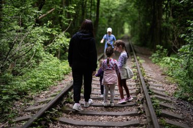 Çevresi çocuklarla çevrili bir orman raylarında yürüyen bir aile.