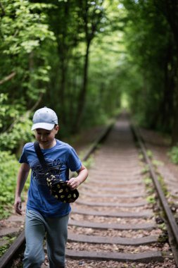Çocuk ıssız bir demiryolu hattını geçiyor, sakin, yeşil ormanlık bir alanda, açık havada..