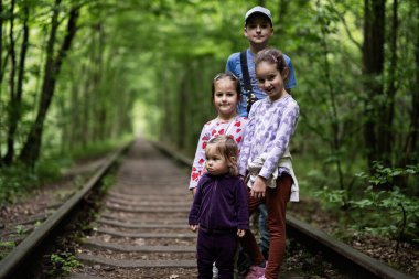 Dört çocuk, yemyeşil ormanlarla çevrili eski bir demiryolunda poz veriyor.