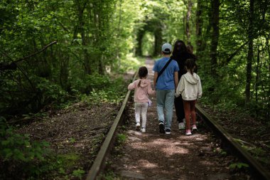 Yeşilliklerle çevrili manzaralı bir yolda yürüyen bir grup insan.