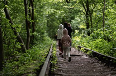 Çocuklar uzun yeşil ağaçlarla çevrili sessiz bir tren yolunda geziniyorlar.