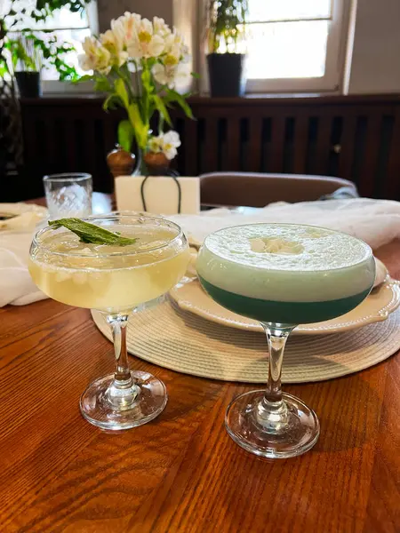 Ahşap bir masada iki kokteyl. Etrafı rahat ve şık iç dekorasyonlarla çevrili.