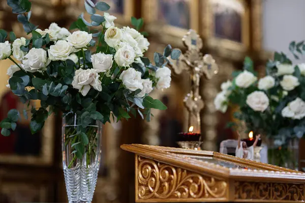 Haçın yanındaki vazolarda güzel beyaz güller ve süslü bir sunakta mumlar..