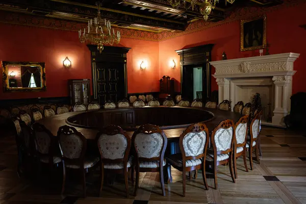 Zbarazh, Ukrayna - 30 Mayıs 2025: Dairesel ahşap masa, sandalyeler, avize ve karmaşık ayrıntıların yer aldığı klasik tarz oda