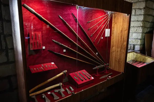 Zbarazh, Ukrayna - 30 Mayıs 2025: Kırmızı ve ahşap dekorlu bir müze sergisinde sergilenen antik silahlar ve aletler