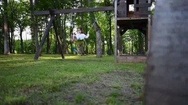 Mutlu çocuklar yaz boyunca parkta salıncaklarda oynuyorlar. Çocukluk anıları ve tasasız eğlence.