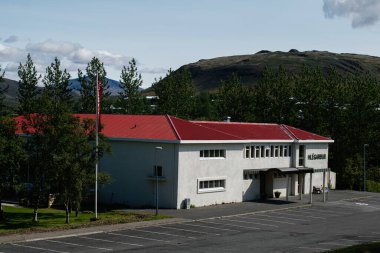 Mosfellsbr, İzlanda - Haziran 2025: Mosfellsbr, İzlanda 'da ağaçların ve dağların ortasında kırmızı çatılı beyaz bina